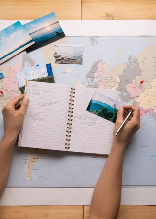 Above view of unrecognizable woman sitting at table with world map and making notes about sights